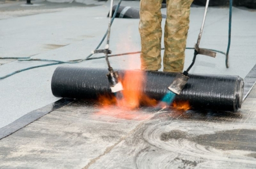 Roofing felt installation with heating and melting roll of bitumen roll by torch on flame